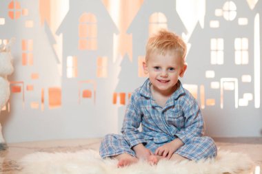 Sevimli sarı saçlı küçük çocuk pijama yakınındaki Noel oyuncak kağıt evler.