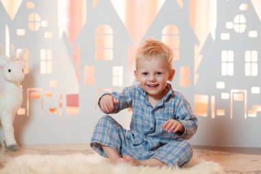 Sevimli sarı saçlı küçük çocuk pijama yakınındaki Noel oyuncak kağıt evler.