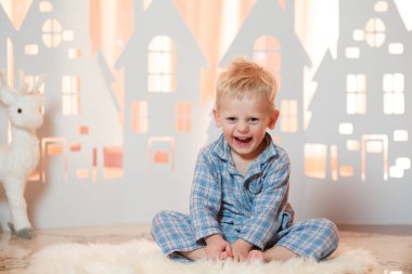 Sevimli sarı saçlı küçük çocuk pijama yakınındaki Noel oyuncak kağıt evler.