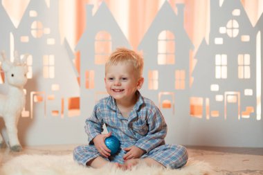 Sevimli sarı saçlı küçük çocuk pijama yakınındaki Noel oyuncak kağıt evler.