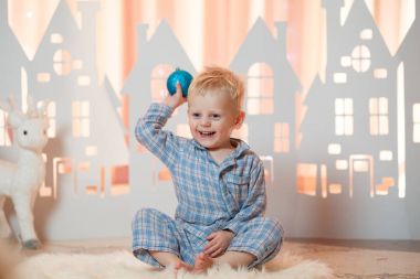 Sevimli sarı saçlı küçük çocuk pijama yakınındaki Noel oyuncak kağıt evler.