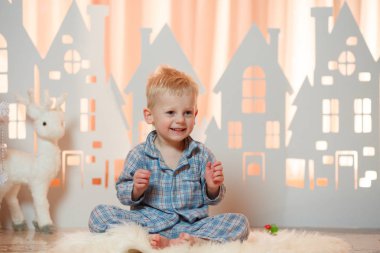 Sevimli sarı saçlı küçük çocuk pijama yakınındaki Noel oyuncak kağıt evler.
