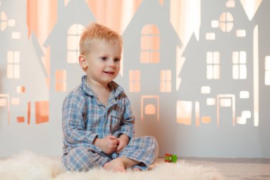 Sevimli sarı saçlı küçük çocuk pijama yakınındaki Noel oyuncak kağıt evler.