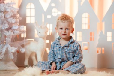 Sevimli sarı saçlı küçük çocuk pijama yakınındaki Noel oyuncak kağıt evler.