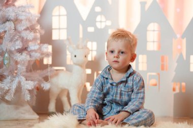 Sevimli sarı saçlı küçük çocuk pijama yakınındaki Noel oyuncak kağıt evler.