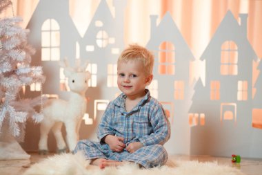 Sevimli sarı saçlı küçük çocuk pijama yakınındaki Noel oyuncak kağıt evler.
