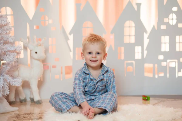 Sevimli sarı saçlı küçük çocuk pijama yakınındaki Noel oyuncak kağıt evler.