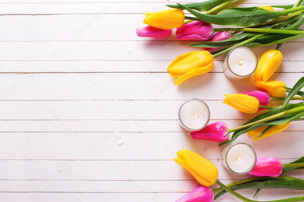 Bright pink and yellow tulips  flowers and candles  on white woo