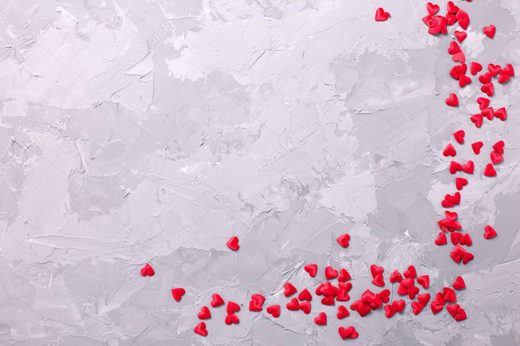 Many little  decorative red hearts on textured grey background. 