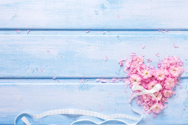 Coração feito de flores rosa e pétalas em tábuas de madeira azul — Fotografia de Stock