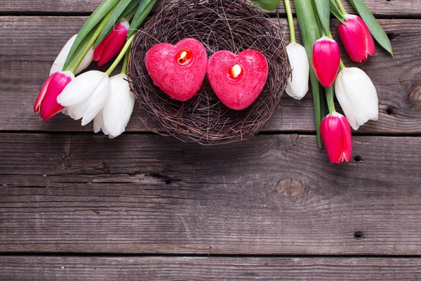 Two red burning candles in nest and bright spring tulips — Stock Photo, Image