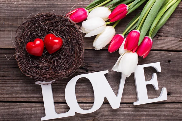 Palabra de amor, dos corazones rojos en nido y brillantes flores de primavera — Foto de Stock