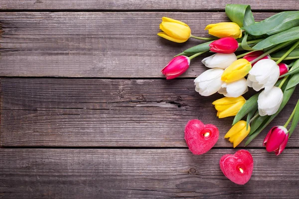 Dvě červené hořící svíčky ve tvaru srdce a tulipány — Stock fotografie
