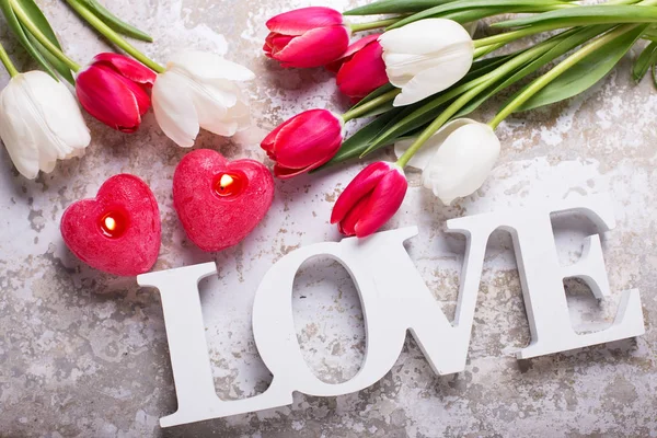 Woord liefde, kaarsen en heldere bloemen — Stockfoto