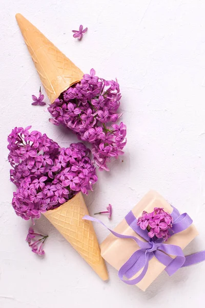 Splendid lilac flowers in waffle cones in box with present on grey textured background. Top view with copy space