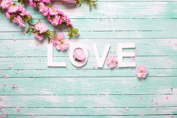 Word love and  border from pink almond flowers on turquoise wooden background. Love concept. Selective focus. Place for text.