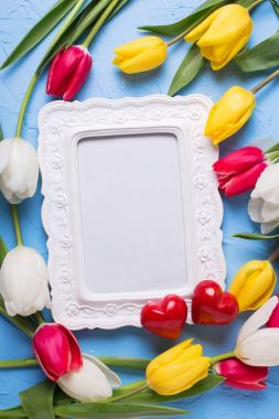 Boş çerçeve metin, iki kırmızı kalp ve mavi dokulu arka plan üzerinde kırmızı, sarı ve Beyaz Lale çiçekler için. Seçici odak. Metin için yer. Düz yatıyordu