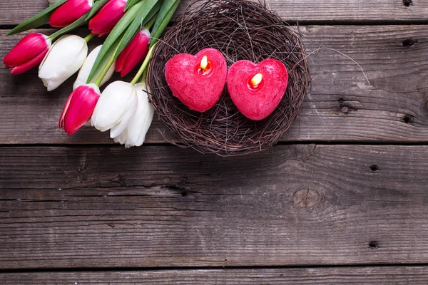 Dvě Červené Hořící Svíčky Podobě Srdce Hnízdě Jarní Květiny Tulipány — Stock fotografie