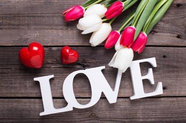 Kelime aşk, iki kırmızı kalp, ahşap arka plan üzerinde parlak bahar çiçekleri. Üstten Görünüm.