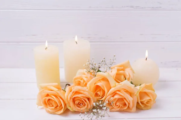 Candles and peach color roses on white wooden background