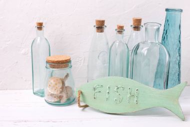 Okyanus ya da deniz Tema ev dekorasyonu. Dekoratif ahşap balık, şişe, kabukları beyaz dokulu arka plan üzerinde. Seçici odak. Metin için yer.