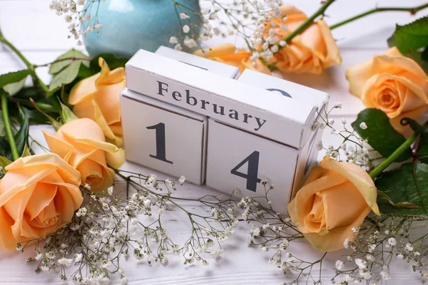 Holiday 14 February background with flowers. Peach color roses flowers and calendar on white wooden planks. Top view.