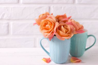 Beyaz duvar karşı Beyaz ahşap zemin üzerinde mavi bardak taze turuncu gül. Metin için yer. Çiçekli natürmort.