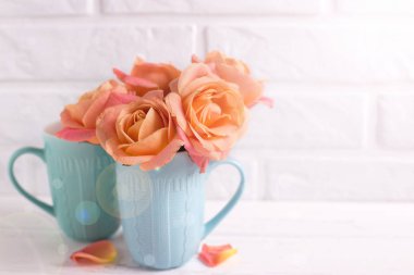 Beyaz ahşap arka plan beyaz duvara ışık hüzmesi içinde mavi bardak taze turuncu gül. Metin için yer. Çiçekli natürmort.