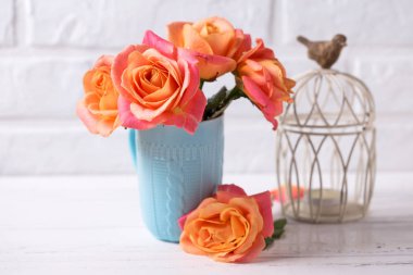 Mavi kupa ans mum beyaz duvara Beyaz ahşap zemin üzerinde taze turuncu gül. Metin için yer. Çiçekli natürmort.