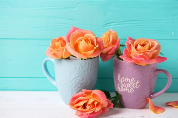 Bunch of fresh orange roses  in cups against  turquoise  wall. Place for text. Floral still life.