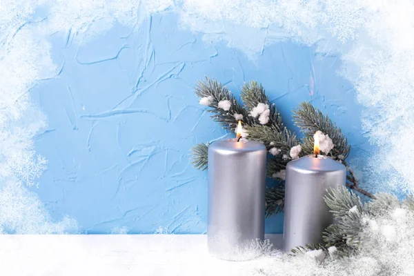 Christmas background. Silver candles and  branches fur tree  on  white  background against  blue wall. Selective focus is on candles.