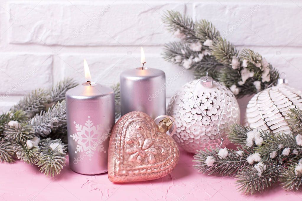 Silver candles, branches fur tree and balls on pink  background against  white wall. Place for text. Selective focus.