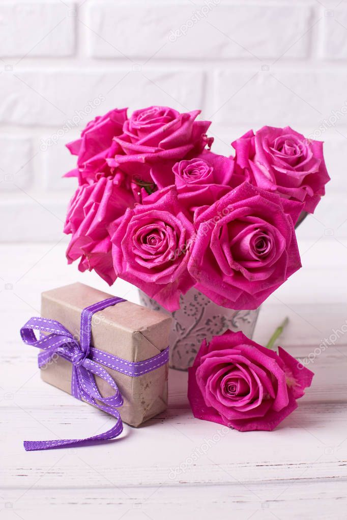 Bright pink roses flowers in pot  and box with present  on white  wooden background. Selective focus. Vertical image.