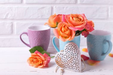 Mavi Kupası ve beyaz duvara Beyaz ahşap zemin üzerinde dekoratif kalp taze turuncu gül. Çiçekli natürmort. Seçici odak.