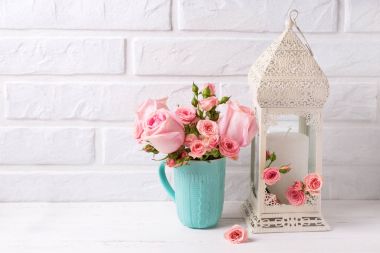 Pembe Gül çiçek mavi Kupası ve dekoratif beyaz fener beyaz duvara karşı. Çiçekli natürmort. Seçici odak. Metin için yer. 