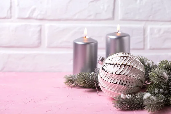 Big white ball, silver candles and  branches fur tree on pink  background against  white wall. Place for text. Selective focus.