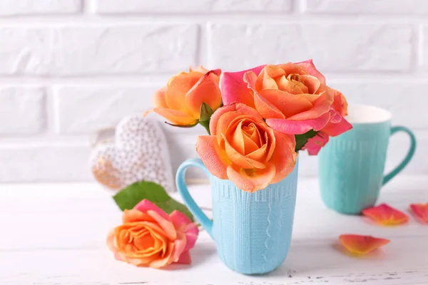 花の静物画 ブルーのカップと白い壁に白い木製の背景に装飾的な心で新鮮なオレンジ色のバラ — ストック写真
