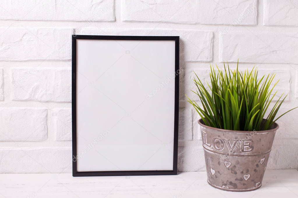 Empty frame mockup  with copy space and  grass in pot  near by brick white wall. 