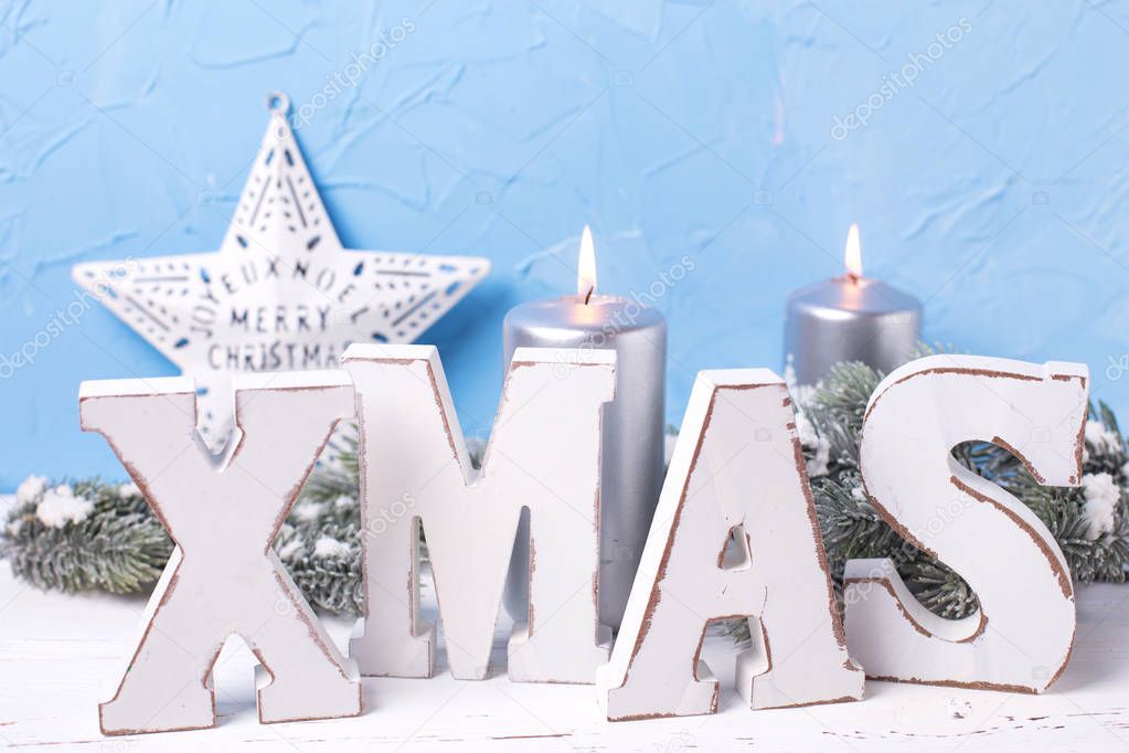 Wooden word Xmas,  silver candles, branches fur tree and star on  white background against   blue wall. Selective focus.