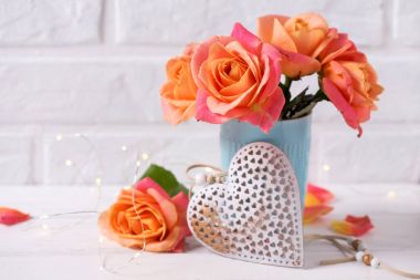 Mavi Kupası ve beyaz duvara Beyaz ahşap zemin üzerinde dekoratif kalp taze turuncu gül. Çiçekli natürmort. Seçici odak.