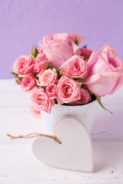 Pembe Gül beyaz pot ve menekşe duvara beyaz kalp çiçeklenir. Çiçekli natürmort. Seçici odak. Dikey görüntü.