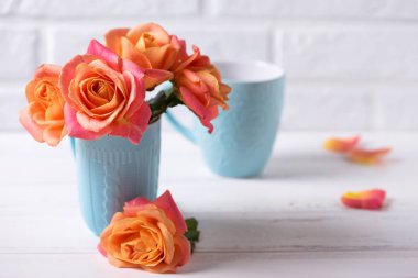 Çiçekli natürmort. Taze Gül beyaz duvara Beyaz ahşap zemin üzerinde mavi Kupası'nda. Metin için yer. Seçici odak.