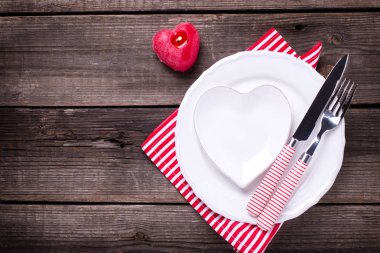St Sevgililer günü sofra. Beyaz tabak içinde kalp, kırmızı mum, çatal ve peçete yaşlı ahşap kağıt üzerinde. Seçici odak. Metin için yer.