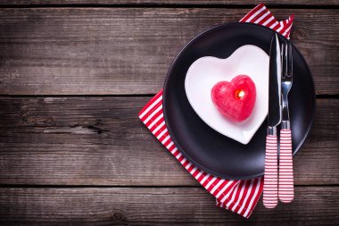 St Sevgililer günü sofra. Siyah saç, beyaz tabak içinde kalp, kırmızı mum, çatal ve peçete yaşlı ahşap kağıt üzerinde. Seçici odak üzerinde çatal olduğunu. Üstten Görünüm.