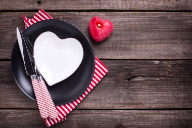 St Sevgililer günü sofra. Siyah saç, beyaz tabak içinde kalp, kırmızı mum, çatal ve peçete yaşlı ahşap kağıt üzerinde. Seçici odak. Metin için yer