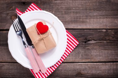 St Sevgililer günü sofra. Beyaz tabak, hediye kutusu, çatal ve peçete ahşap arka plan üzerinde. Seçici odak. Metin için yer.