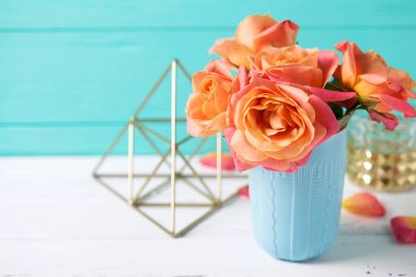 Bunch of fresh orange roses in blue cup on white wooden background against  turquoise  wall. Place for text. Floral still life. clipart