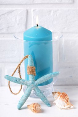 Yanan mum, kabukları ve deniz yıldızı yakınındaki beyaz tuğla duvar tarafından mavi. Seçici odak. Dikey görüntü.