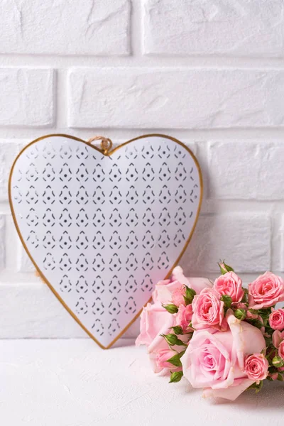 Wedding background. Bunch of tender pink roses flowers and  heart against  white brick wall. Floral still life.  Selective focus. Place for text. Vertical image.