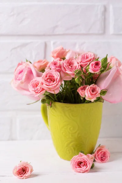 粉红色的玫瑰花在绿色的杯子对白色砖墙 花静物 选择性对焦 文本的位置 垂直图像 — 图库照片